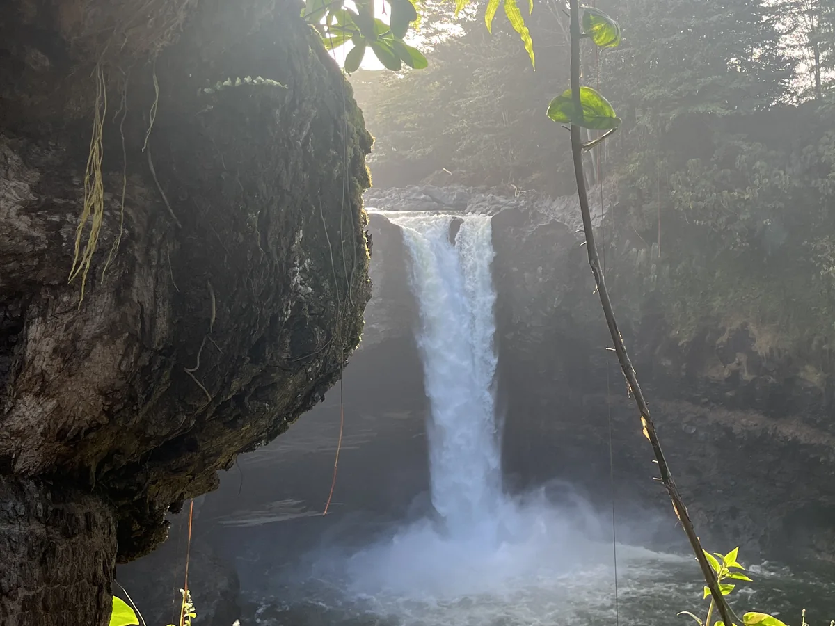 Rainbow Falls seen from the shaded cave overlook, sunlight breaking through the mist