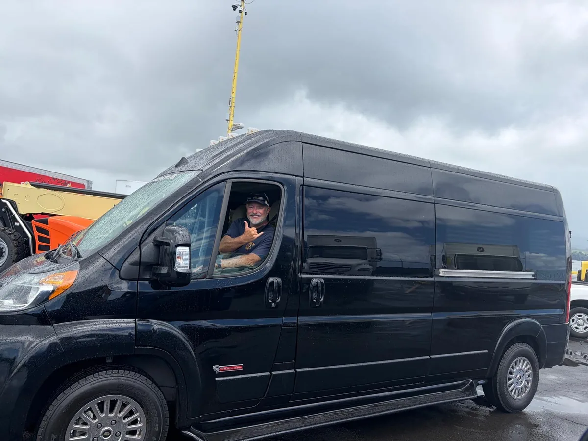 The black high-roof accessible van with its driver giving a shaka from the window